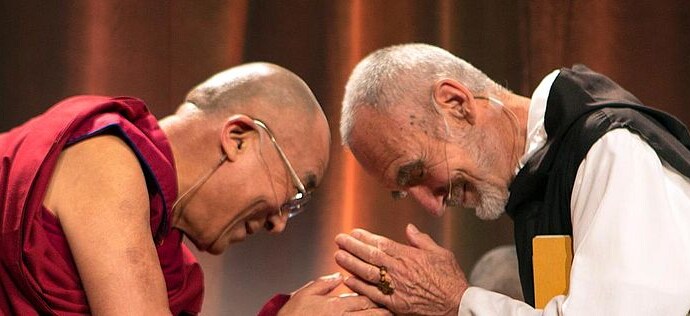 The Dali Lama and another man bow towards each other smiling in a gesture of respect.
