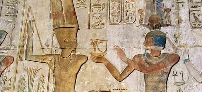 Egyptian reliefs on a stone wall. The figures are painted. There are four people. Two men, one woman, and the other is a god.